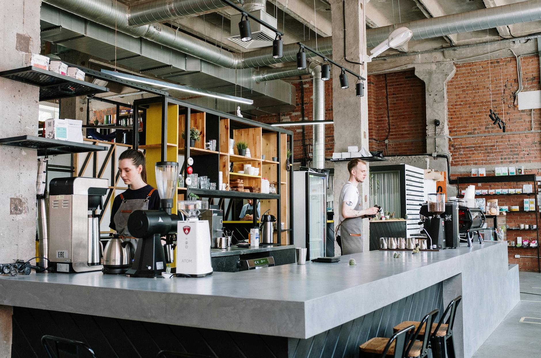Baristas working in a trendy industrial-style coffee shop with exposed brick and beams.